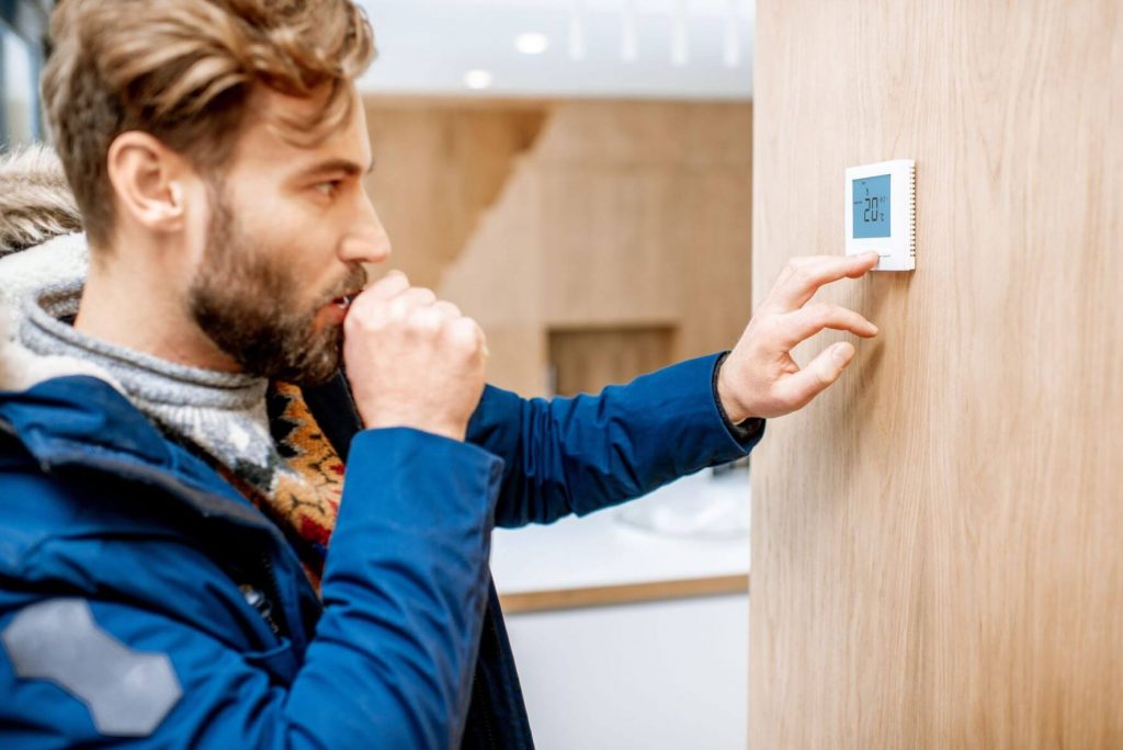 Guy that is cold in blue jacket looking at thermostat